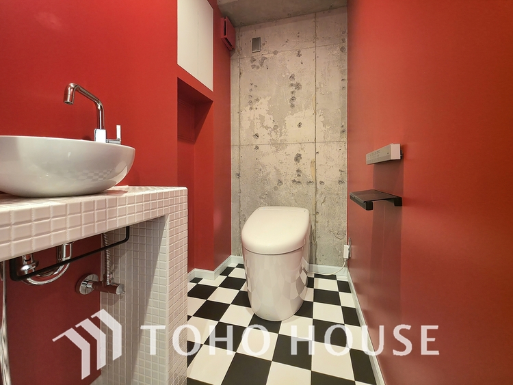 トイレ 鮮やかな赤の壁とコンクリート打ちっ放し、市松模様の床が個性的なトイレです。デザイン性の高いボウル型手洗い器も完備され、訪れる人に強烈なインパクトを与えます。