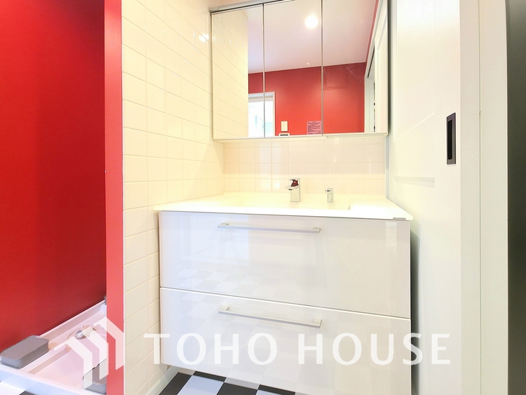 洗面 鮮やかな赤の壁と市松模様の床が印象的な洗面所です。三面鏡の裏には収納があり、洗面台の下も引き出し式で、機能性とデザイン性を兼ね備えています。