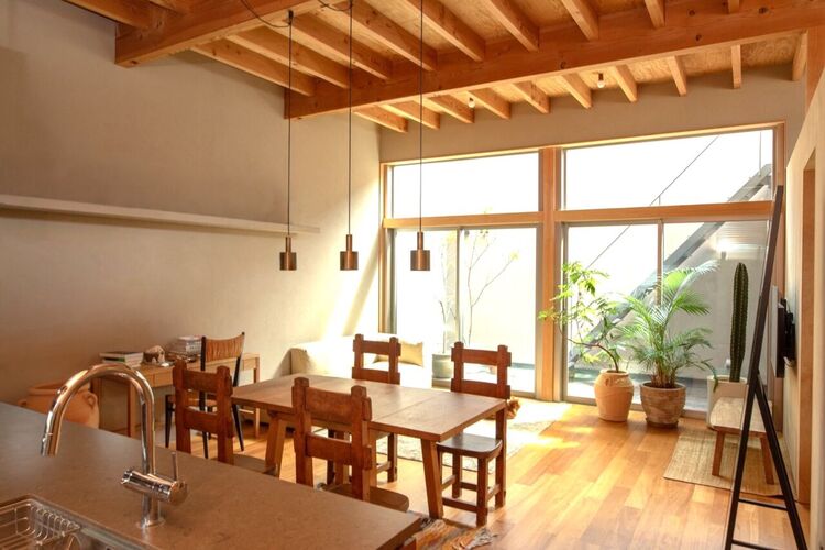 居間 吹抜け天井と大開口が生む圧倒的な開放感。無垢材の梁と木質の温もりに包まれ、光と緑が調和する上質なLDK空間。設計美と居心地を兼ね備えた、日常を格上げする住まいの中心です。